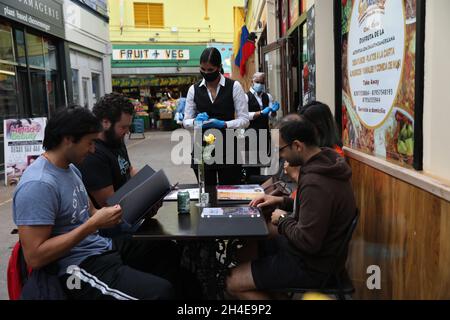 Une serveuse portant un masque facial et des gants de protection sert les clients assis au restaurant colombien, Santafereno, dans le marché du village de Brixton, dans le sud de Londres, ouvrant leurs portes pour la première fois en trois mois après une détente majeure des restrictions de verrouillage du coronavirus.Date de la photo : samedi 4 juillet 2020. Banque D'Images