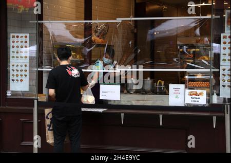 Un client est servi par un écran en plastique, par un assistant-boutique portant un EPI, comme mesure de précaution pour contrôler la propagation du coronavirus dans Chinatown à Londres. Date de la photo: Jeudi 9 juillet 2020. Banque D'Images