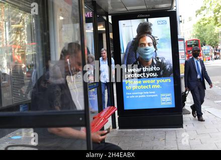 Un homme portant un visage couvrant des promenades passe devant un écran sur un arrêt de bus à Londres affichant un avis du NHS indiquant aux voyageurs de porter un masque de protection pour leur sécurité dans les transports publics, car les revêtements de visage deviennent obligatoires dans les transports publics en Angleterre.Date de la photo : vendredi 7 août 2020. Banque D'Images