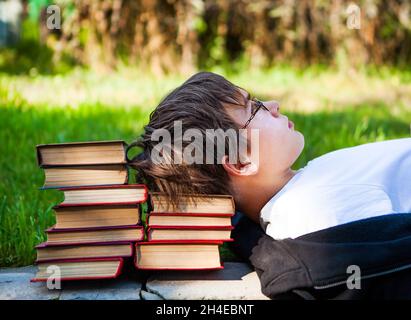 Adolescent fatigué couché sur les livres dans le parc Banque D'Images
