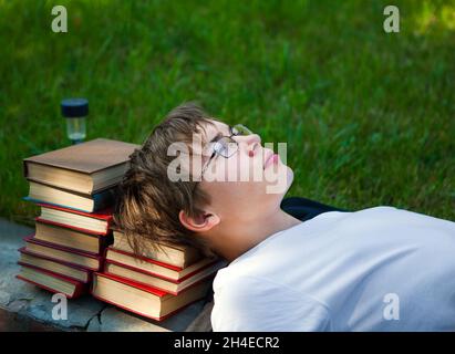 Adolescent fatigué couché sur les livres dans le parc Banque D'Images