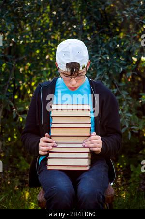 Triste adolescent avec un livre assis sur la chaise sur le fond de la nature Banque D'Images