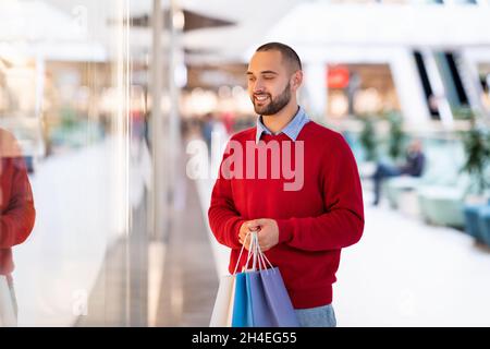 Shopping à la fenêtre.Un bon homme de race blanche qui regarde la vitrine du magasin, tient des sacs en papier avec des achats dans le centre commercial de la ville Banque D'Images