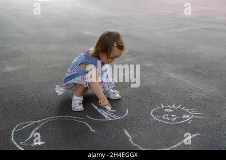 Photo aérienne d'une petite fille cribblant dans la craie colorée sur le trottoir Banque D'Images