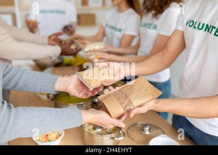De jeunes volontaires donnent des dons alimentaires aux pauvres, en tenant des colis avec des céréales et des pâtes, en gros plan Banque D'Images