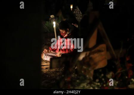 Une personne tient une soirée au cimetière de San Pedro Tláhuac, pour attendre l'arrivée de leurs proches décédés, les parents décorent avec des fleurs,Apportez-leur de la nourriture et chantez-leur aux tombes comme traditions mexicaines du jour des morts pour leur souhaiter un bon retour sur la route de Mictlan.Le 1er novembre 2021 à Mexico, Mexique.(Photo de Fernanda Rojas/ Eyepix Group) Banque D'Images