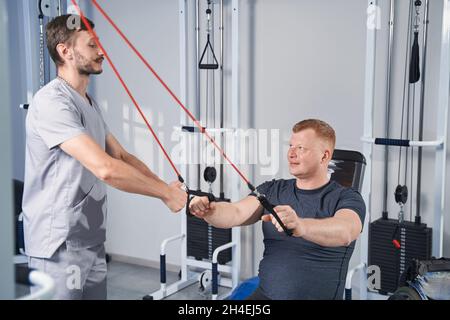 Médecin aider l'homme de paralysie cérébrale faire des exercices avec le simulateur d'étirement Banque D'Images