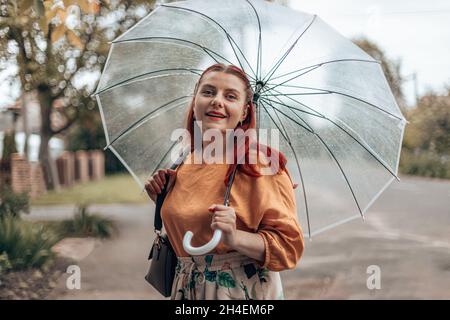 Jeune femme élégante, vêtue de vêtements brillants sous un parapluie transparent par mauvais temps. Banque D'Images