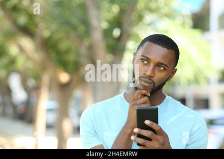 Vue de face portrait d'un homme avec un sking noir tenant le téléphone et pensant dans un parc Banque D'Images