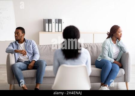 Vue arrière de la psychologue féminine donnant une séance de thérapie au jeune couple noir au bureau, les aidant avec le conflit Banque D'Images