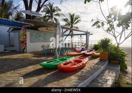 Divers équipements de sports nautiques exposés à l'extérieur d'une boutique de sports nautiques avec plage tropicale et océan Indien en arrière-plan, Diani, Kenya Banque D'Images