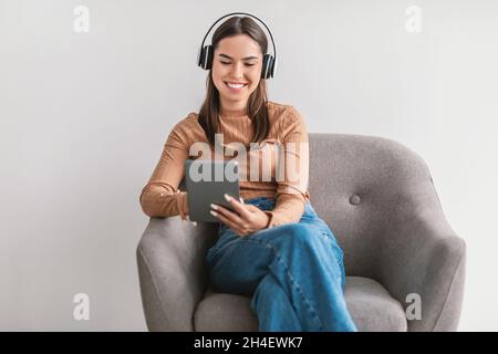 Bonne femme caucasienne ayant un appel vidéo, en utilisant une tablette pc, assis dans un fauteuil avec un casque sur fond blanc Banque D'Images