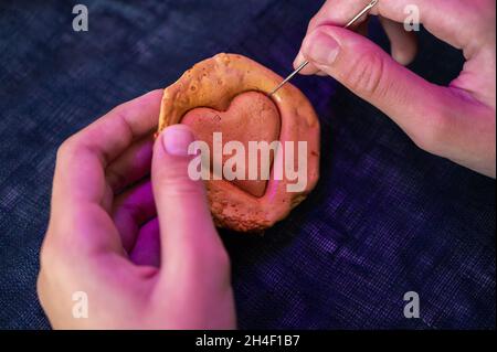 Les mains de gros plan scratch cassent sucre caramel bonbons biscuits avec une aiguille en métal en forme de coeur sur un fond blanc Banque D'Images
