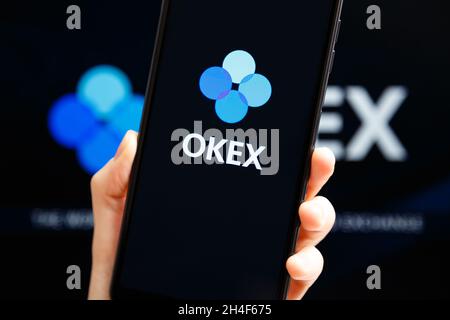 Ukraine, Odessa - octobre, 9 2021: Mains tenant mobile avec l'application OKEx fonctionnant sur l'écran du smartphone avec le logo OKEx en arrière-plan.OKEx est une plate-forme d'échange et de négociation de crypto-monnaies Banque D'Images