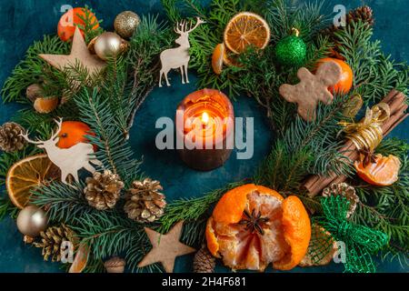 Composition de Noël et du nouvel an sur fond vert, mandarines, oranges, bougies, branches de sapin,cônes, baies, bâtonnets de cannelle Banque D'Images