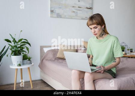 jeune femme avec tatouage utilisant un ordinateur portable tout en étant assis sur le lit à la maison Banque D'Images