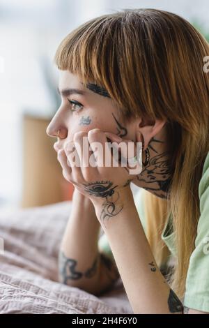 vue latérale de la femme tatouée avec piercing regardant loin sur le lit à la maison Banque D'Images