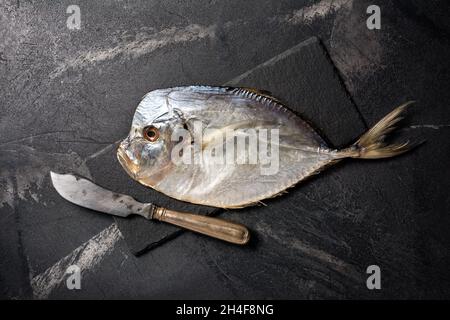 Vue de dessus de savoureux vomissant de poisson de mer salé séché ou Selena avec couteau d'argent sur le tableau d'ardoise et le fond en marbre noir Banque D'Images