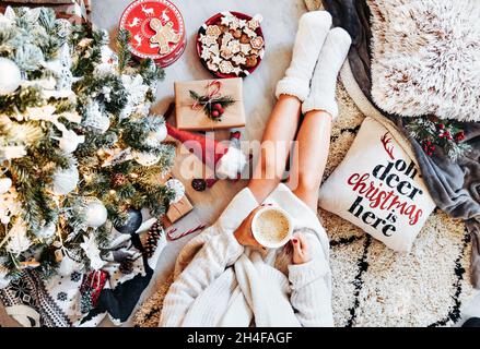 Photo aérienne de la femme tenant une tasse de café ou de cacao, assise près de l'arbre de noël et présente. Banque D'Images