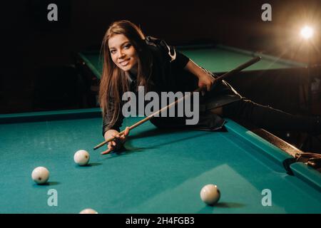 Une fille avec un repère dans ses mains fait un tir à une balle dans un club de billard.Russian billard. Banque D'Images