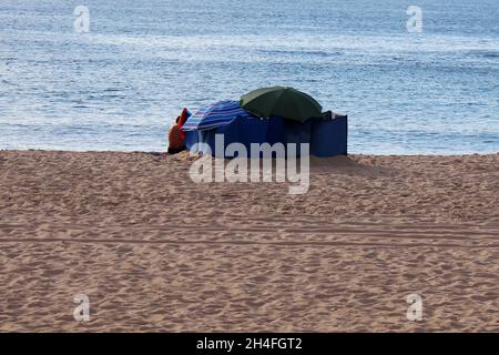 Der Rücken eines Mannes (keine Erkennbarkeit), Sonnenschirme und Beach Wind Screen Windschutz am Strand von Espinho, Portugal. Banque D'Images