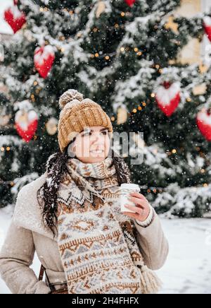 Portrait d'une jeune femme portant des vêtements d'hiver élégants par temps neigeux en ville, buvant du café à emporter Banque D'Images
