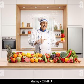 Chef d'un homme mature dans une cuisine avec une pile de fruits et légumes et poivrons dans sa main Banque D'Images