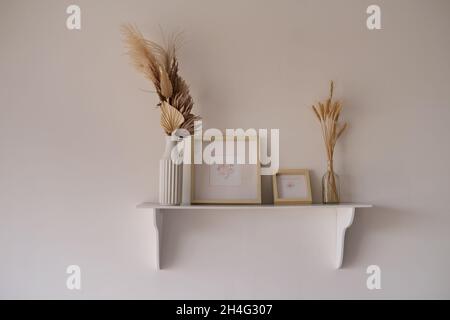 Étagère blanche avec chevalets et fleurs sèches et cadres de maquette avec dessins.Décoration élégante Banque D'Images