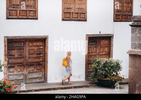 Une blonde dans une sundress avec un sac à dos marche le long de la rue de la vieille ville de Garachico sur l'île de Tenerife.Espagne, îles Canaries Banque D'Images