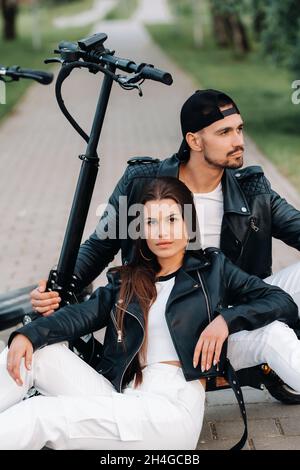 Portrait d'un couple assis près des scooters électriques, appréciant le temps dans la nature ensemble, deux amoureux sur les scooters électriques.personnes sur les scooters. Banque D'Images