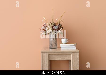 Vase avec de belles fleurs séchées, des livres et une tasse sur la table près du mur beige Banque D'Images