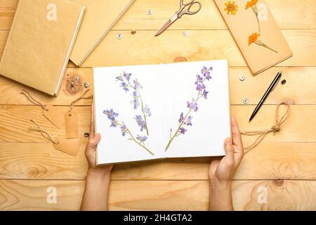 Mains de femmes avec fleurs séchées pressées dans le livre sur fond de bois Banque D'Images