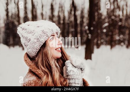 Photo de jeune belle femme en fourrure debout sur la neige blanche en forêt d'hiver.La fille est souriante et heureuse avec les yeux fermés.La femme a l'hiver Banque D'Images