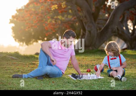 École d'échecs pour enfants.Une famille heureuse à l'extérieur.Père et fils jouant aux échecs dans le jardin de printemps. Banque D'Images