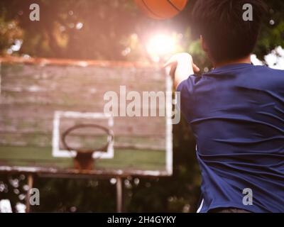 Un adolescent tient un ballon de basket-ball et jette le ballon dans un panier sur un terrain en plein air. Banque D'Images