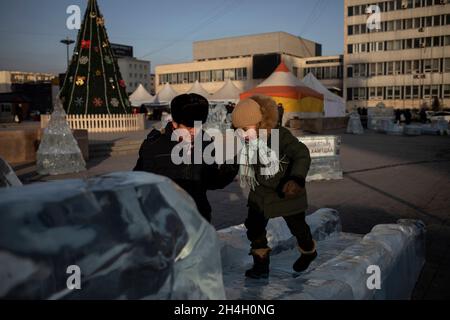 Un père joue avec son enfant sur une sculpture sur glace dans la capitale Oulan-Bator, le 22 janvier 2019.Avec des températures enregistrées chutent à -40 degrés Banque D'Images