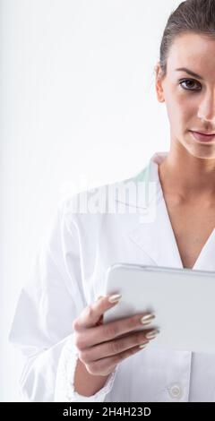 Demi-portrait d'une femme médecin ou infirmière en blouse de laboratoire blanche tenant un PC tablette et regardant la caméra avec une expression sérieuse Banque D'Images