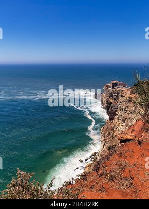 Vue sur les falaises jusqu'au phare de Farol de Nazaré et l'océan Atlantique, Praia do Norte, Nazaré, Portugal Banque D'Images