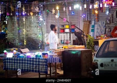 Homme sur le petit stand de bord de route orné de lumières suspendues colorées les vendant pour le festival hindou de diwali Banque D'Images