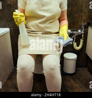 La femme nettoie la salle de bains de la maison.Désinfection avec des gants en caoutchouc jaune dans les toilettes Banque D'Images