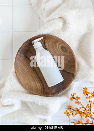 Bouteille en plastique blanc avec pompe, utilisée pour le savon liquide, le shampooing et la lotion sur le plateau en bois sur fond de carreaux blancs.Vue de dessus Banque D'Images