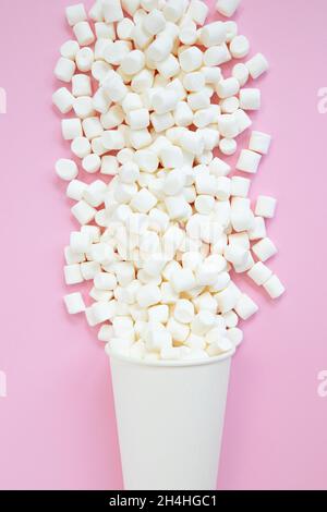 les petits guimauves blanches sont saupoudrées d'une tasse en papier isolée sur un fond rose festif Banque D'Images