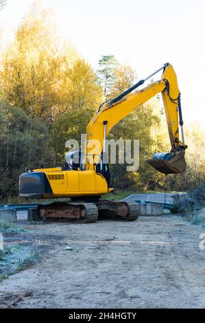 une excavatrice sur chenilles jaune attend tôt le matin des travaux d'excavation sur la route près de la forêt d'automne Banque D'Images