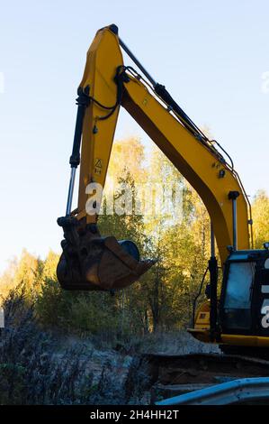 une excavatrice sur chenilles jaune attend tôt le matin des travaux d'excavation sur la route près de la forêt d'automne Banque D'Images