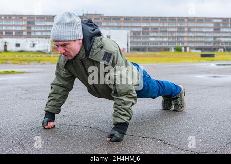 Un athlète en automne froid est engagé dans la forme physique à l'extérieur, effectuant des exercices de base pour renforcer les muscles de la poitrine Banque D'Images