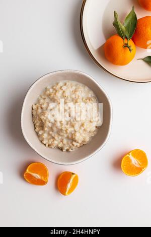 Porridge de flocons d'avoine maison avec tranches de fruits de mandarine ou de clémentine sur fond blanc.Fond de fruit coloré.Flat lay, vue de dessus, espace de copie. Banque D'Images