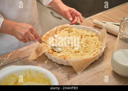 Une femme adulte en vêtements blancs de chef cuisant une tarte dans une cuisine beige. Banque D'Images