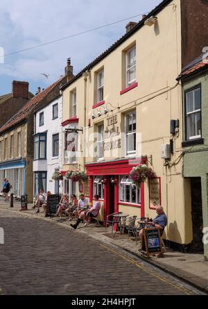 Une journée d'été avec des touristes sur la grande rue principale avec des boutiques et des pubs dans le village de bord de mer de Staithes dans le North Yorkshire, Angleterre. Banque D'Images