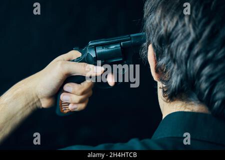 Guy se suicide avec coup de balle dans la tête.Homme déprimé avec un pistolet près d'un mur sombre. Banque D'Images