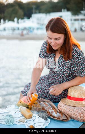 Jeune heureuse belle femme assise sur la jetée par la mer.Pique-nique au bord de la mer ou de l'océan dans un coucher de soleil.Vacances Banque D'Images